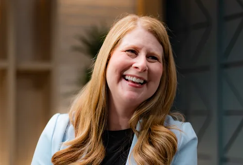 Laughing woman with long strawberry-blonde hair wearing a light blue blazer over a black top